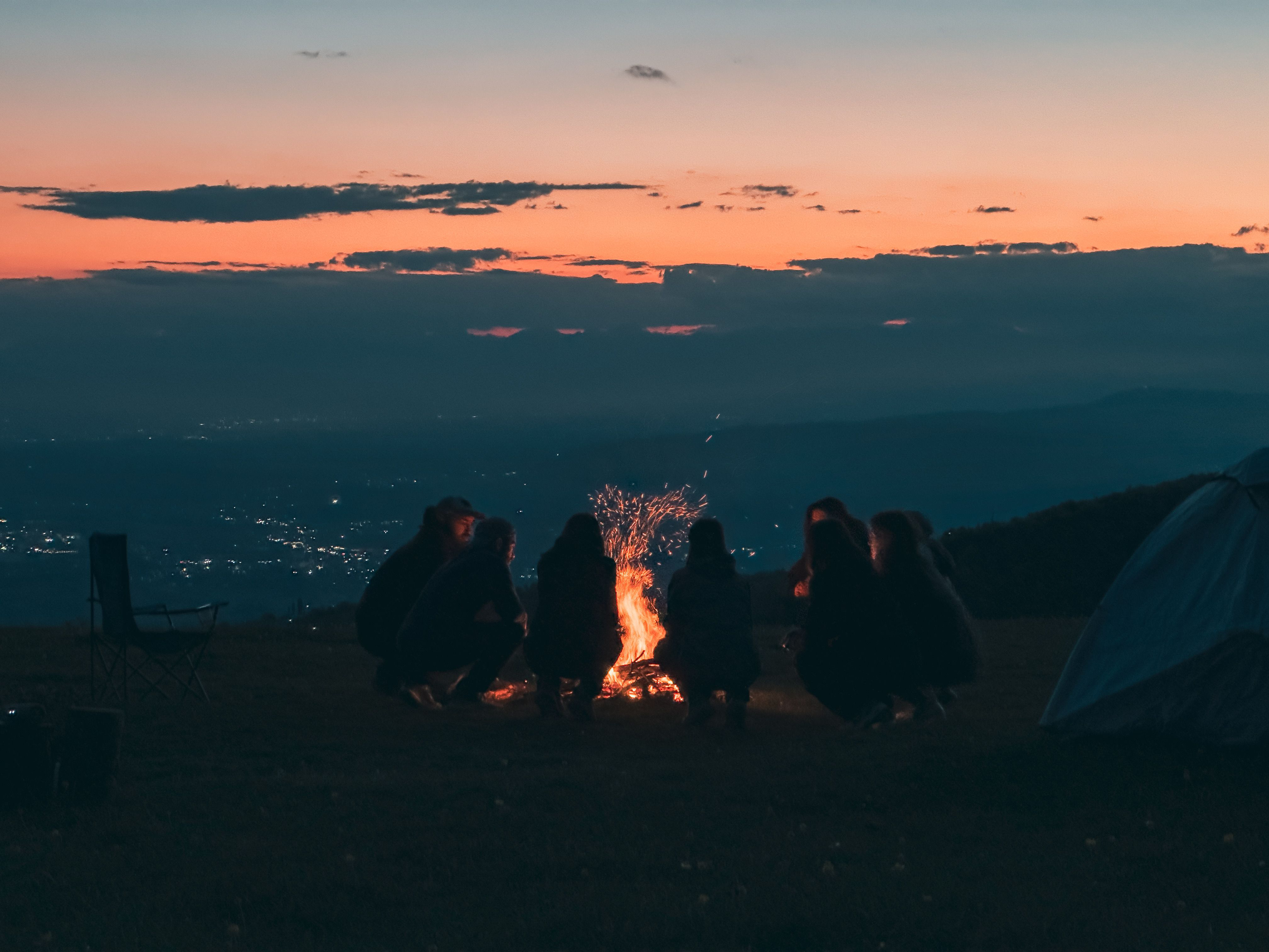 Eine Gruppe Menschen sitzt in der Abenddämmerung um ein Lagerfeuer und erzählt sich Geschichten