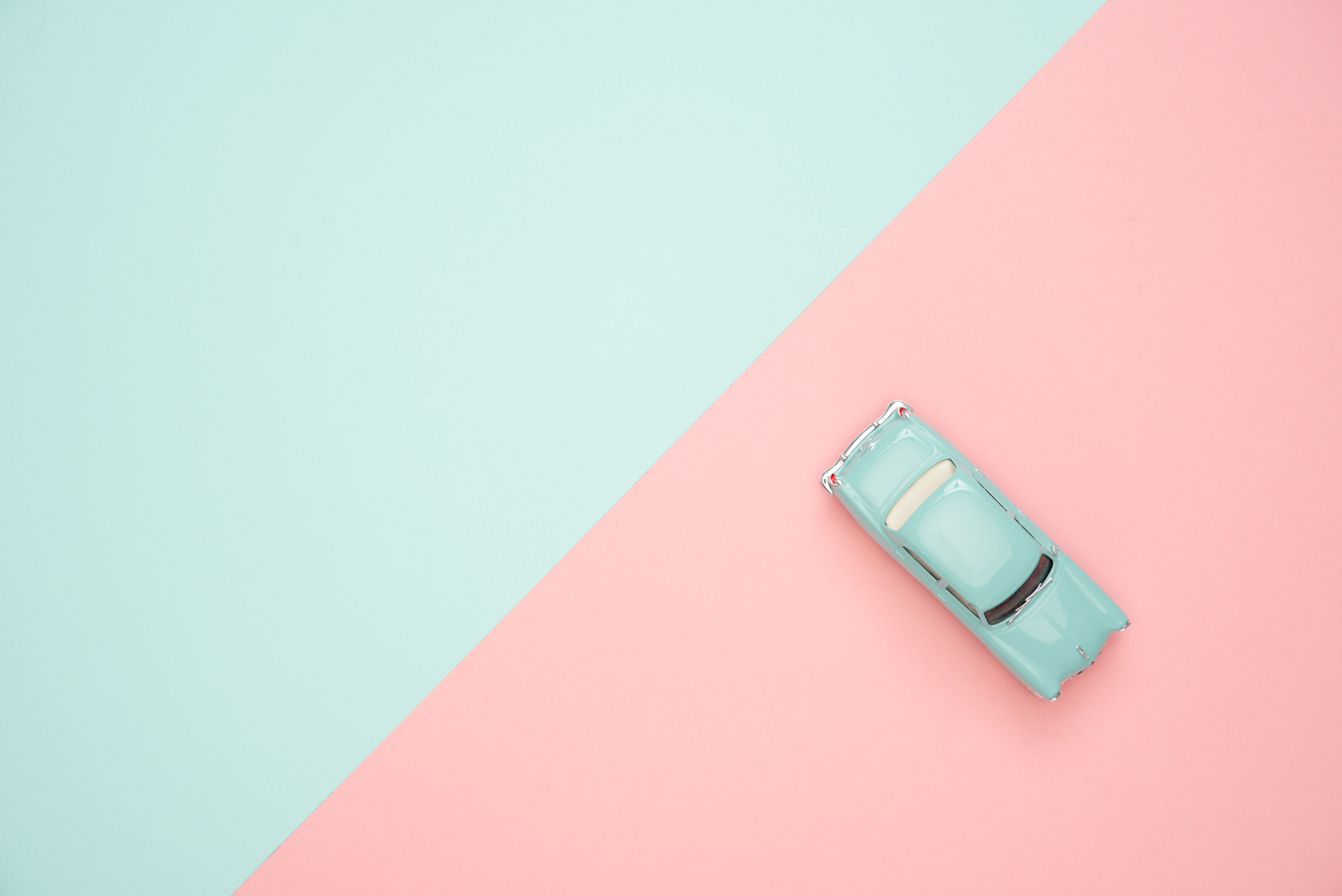 Türkisfarbenes Spielzeugauto im Retrostil auf einem zweifarbigen Hintergrund in Mint und Rosa